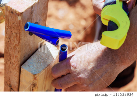 Plumber using saw tools to cut plastic blue PVC water piping system 115538934