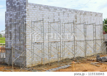 During construction, mason makes concrete wall from cement blocks while standing on scaffold 115538943