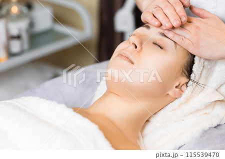Young woman enjoying facial massage, lying on spa bed indoor at beauty salon. Young woman enjoying facial massage, lying on spa bed indoor at beauty salon. 115539470