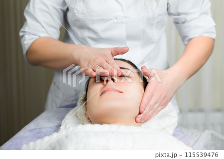 Young woman enjoying facial massage, lying on spa bed indoor at beauty salon. Young woman enjoying facial massage, lying on spa bed indoor at beauty salon. 115539476