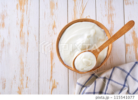 Greek yogurt or sour cream in a wooden bowl with spoon on a light table, top view. 115541077