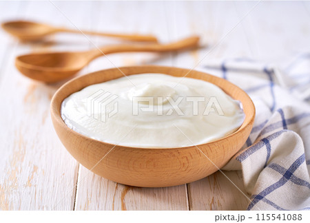 homemade organic yogurt in a wooden bowl with spoon on a white table, selective focus. homemade organic yogurt in a wooden bowl with spoon on a white table, selective focus. 115541088
