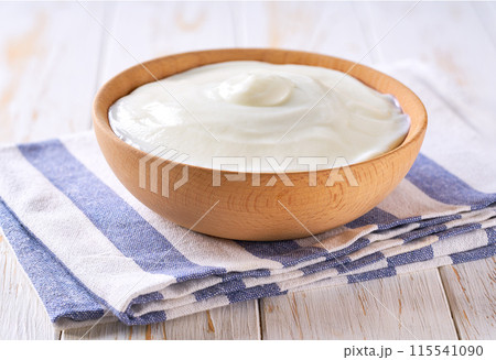 tasty greek yogurt in a wooden bowl on a white table, selective focus. tasty greek yogurt in a wooden bowl on a white table, selective focus. 115541090