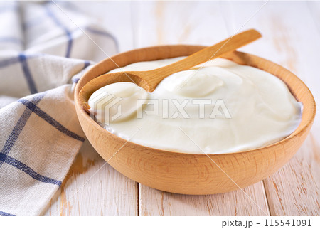 Natural yogurt in a wooden bowl with spoon on a light background, selective focus. 115541091