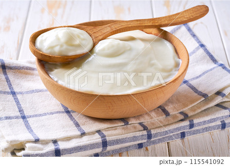 homemade organic yogurt in a wooden bowl with spoon on a light table, selective focus. homemade organic yogurt in a wooden bowl with spoon on a light table, selective focus. 115541092