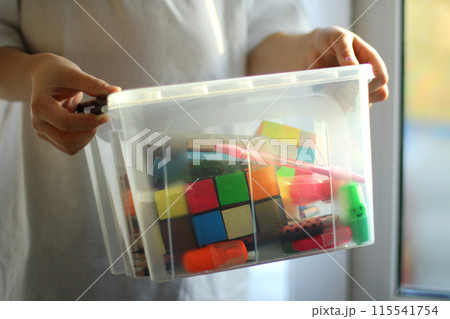 the child holds a box with educational games, puzzles, pencils. preparation for a creative activity the child holds a box with educational games, puzzles, pencils. preparation for a creative activity 115541754