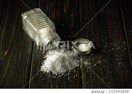Scattered pile of salt from a salt shaker on a black vintage table. Concept of excessive salt consumption, which may be the cause of diabetes or other diseases Scattered pile of salt from a salt shaker on a black vintage table. Concept of excessive salt consumption, which may be the cause of diabetes or other diseases 115541839