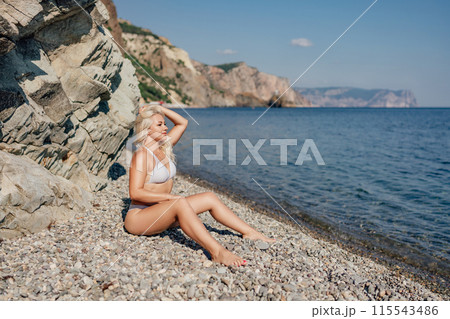 A blonde woman is sitting on a beach with her hair in her hand 115543486