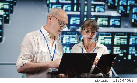Focused IT inspectors looking around data center, using laptop and tablet to crosscheck disaster recovery plan and assess high tech establishment units in need of replacement, preventing perils Focused IT inspectors looking around data center, using laptop and tablet to crosscheck disaster recovery plan and assess high tech establishment units in need of replacement, preventing perils 115544063