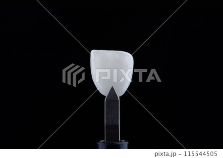 Close up shot ultra thin dental ceramic veneer is held with tweezers with black background. 115544505