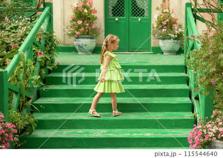 A girl in a green dress in the gardens of Claude Monet in Giverny. Facade of the Monet's house 115544640
