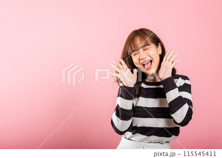 In a studio shot on a pink background, a jubilant Asian woman raises her fists in celebration, expressing success and happiness with a bright smile. 115545411