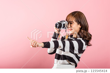 Attractive energetic happy Asian portrait beautiful cute young woman teen excited smiling holding vintage photo camera and pointing finger to side space, studio shot isolated on pink background Attractive energetic happy Asian portrait beautiful cute young woman teen excited smiling holding vintage photo camera and pointing finger to side space, studio shot isolated on pink background 115545414
