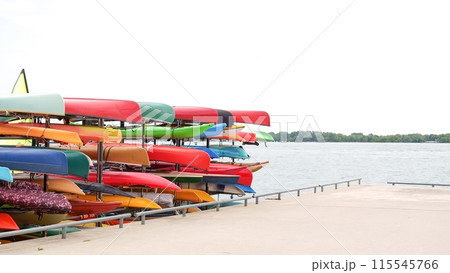 A variety of kayaks and canoes are stacked on a rack near a lake. 115545766