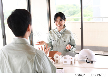 建設模型の前で会議をする作業服を着た男女 115549292