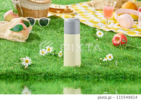 Picnic layout on green grass along the lake scene, from front angle. An unlabeled bottle placed in the middle, dotted with a few tana chrysanthemums, picnic tools decoration in back Picnic layout on green grass along the lake scene, from front angle. An unlabeled bottle placed in the middle, dotted with a few tana chrysanthemums, picnic tools decoration in back 115549814