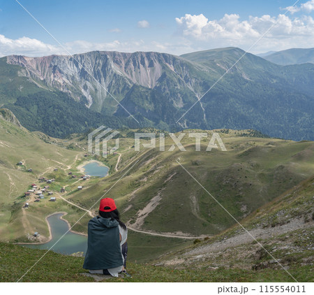 A young woman tourist is resting in the mountains. Mountain landscape panorama. Authentic mountain village with lakes in the gorge. 115554011