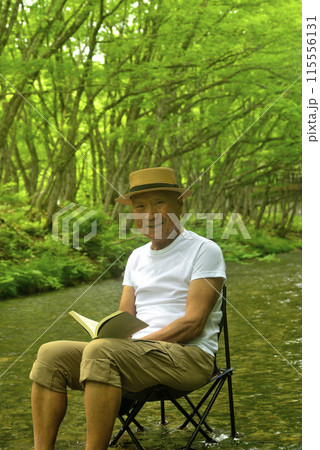 夏に渓流で水に浸かり読書をしながら涼を楽しむシニア男性 夏に渓流で水に浸かり読書をしながら涼を楽しむシニア男性 115556131