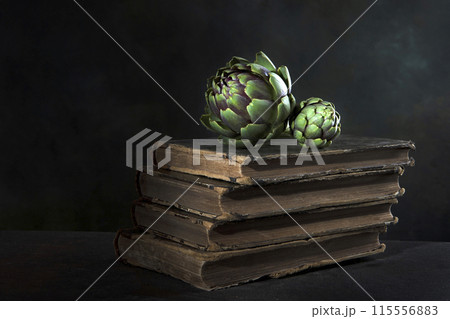 An artichoke and an old book. Artichoke is lying on the book. Dark background. Vintage old book. 115556883