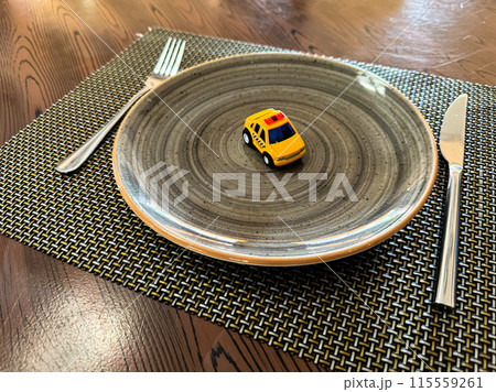 Miniature taxi toy on ceramic plate with cutlery. Concept of calling taxi after end of banquet or celebration. Design of taxi advertising, culinary presentations and unusual concepts. Miniature taxi toy on ceramic plate with cutlery. Concept of calling taxi after end of banquet or celebration. Design of taxi advertising, culinary presentations and unusual concepts. 115559261