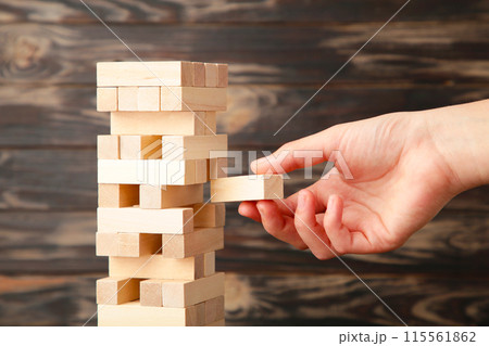 Business woman hand pick and put last piece block of the wood puzzle. Wooden block on brown background Business woman hand pick and put last piece block of the wood puzzle. Wooden block on brown background 115561862