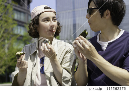 インバウンド　東京駅の前の広場に座っておにぎりを食べる外国人旅行者カップル 115562376