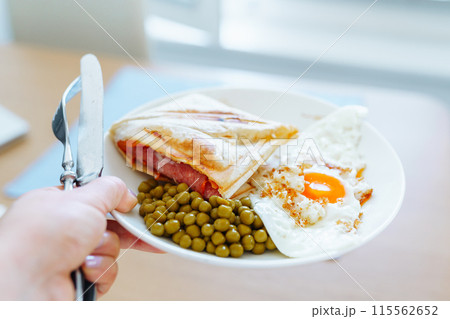 breakfast scrambled eggs hot sandwich with ham and cheese, green peas, legumes on plate breakfast scrambled eggs hot sandwich with ham and cheese, green peas, legumes on plate 115562652
