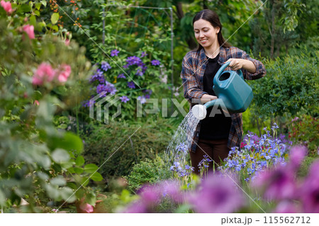 smiling young woman gardener water the flowers and plants from watering can in garden smiling young woman gardener water the flowers and plants from watering can in garden 115562712