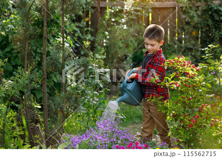 smiling little boy water the flowers from watering can in garden 115562715