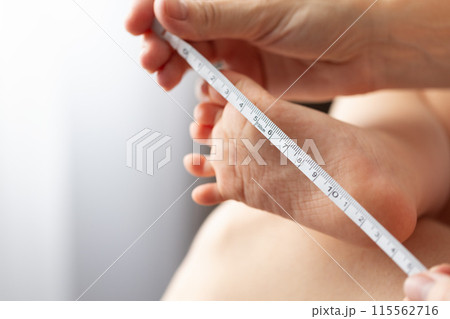Mother measuring with centimetre the foot of her child. Closeup 115562716