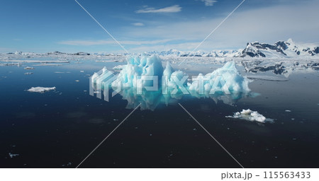 Piece of ice from melting iceberg drifting open ocean in sunny day. Snow covered mountain in background. Ecology, climate change and global warming concept. Polar Antarctica summer landscape. Panorama 115563433