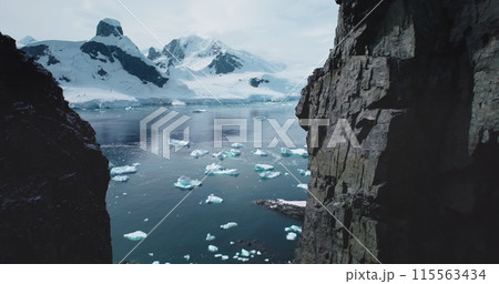 Aerial flight in mountain canyon Antarctica. Majestic snowy mountains towering polar ocean. Cracked glacier icebergs melting floating in cold ocean. Ecology, melting ice, climate change global warming Aerial flight in mountain canyon Antarctica. Majestic snowy mountains towering polar ocean. Cracked glacier icebergs melting floating in cold ocean. Ecology, melting ice, climate change global warming 115563434