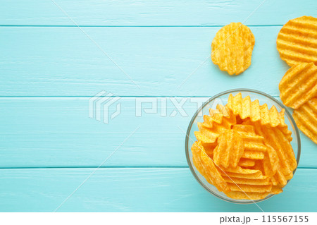 Golden potato chips in bowl on blue wooden background. Golden potato chips in bowl on blue wooden background. 115567155