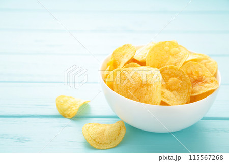 Potato chips on bowl on blue wooden background 115567268