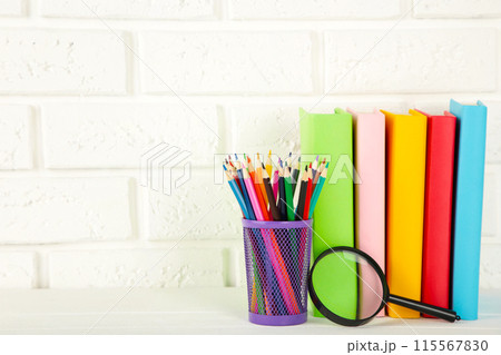 Multi coloured school books and stationery on white brick wall background 115567830