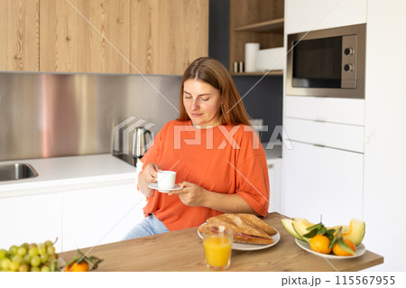 Carefree casual young beautiful happy smiling woman drinking coffee in lazy morning at comfy home interior. Young woman enjoying fresh aromatic coffee in modern kitchen 115567955