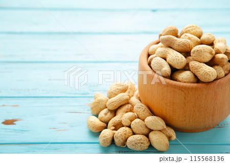 Dried peanuts in wooden bowl on blue wooden background. Dried peanuts in wooden bowl on blue wooden background. 115568136