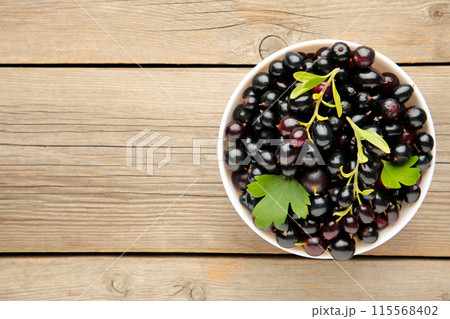 Black currant in a white bowl on grey wooden background Black currant in a white bowl on grey wooden background 115568402