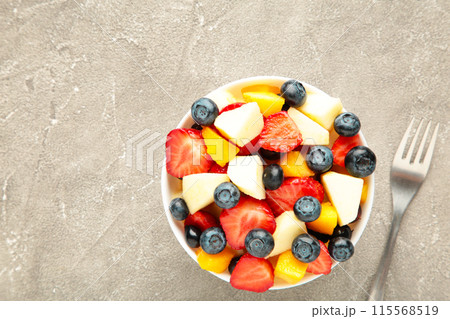 Fruit salad in a bowl with fork, served on grey background. 115568519