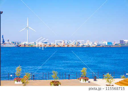 青空の横浜みなとみらいにそびえ立つ風力発電の風車と倉庫と工場・海の景色（神奈川県横浜市） 115568715