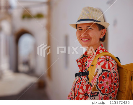 Nice asian Female in boho dress Enjoying Sunny Day on Greek Islands. Travel to Lindos, Mediterranean islands tourist season. Tourist woman on vacation in Greece walking through the streets of Lindos. 115572426