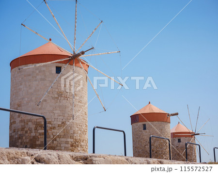 Windmills in the Mandraki port of Rhodes, Greece. Old defensive stands and windmills. Wharf harbors, boats and sailing ships. Historic pier and beach. Travel to Mediterranean islands Rhodes. 115572527