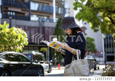 読書しながら街を歩くシニア女性 読書しながら街を歩くシニア女性 115573357