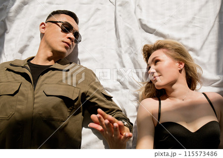 A man and a woman lie on a bed holding hands in the sun A man and a woman lie on a bed holding hands in the sun 115573486