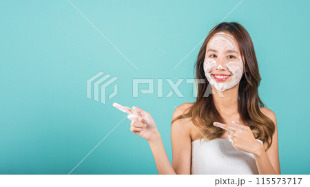 Portrait Asian young woman washing face foaming facewash soap scrub on skin studio shot isolated on blue background, female applying bubble facial foam and cleansing and pointing finger to side away Portrait Asian young woman washing face foaming facewash soap scrub on skin studio shot isolated on blue background, female applying bubble facial foam and cleansing and pointing finger to side away 115573717