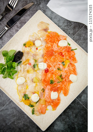 sliced red and white fish with mozzarella cheese and herbs, top view 115574385