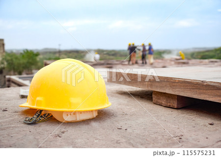 Construction helmet posed with background of workers showing leadership and risk 115575231