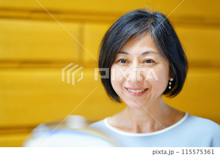 パールピアスを付けて鏡を見る笑顔の中年女性	 115575361