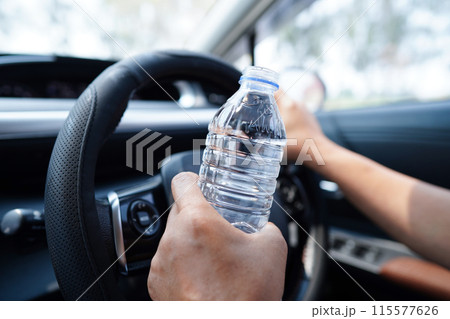 Bangkok, Thailand May 15, 2022 Asian woman driver hold cold water for drink in car, dangerous and risk an accident. Bangkok, Thailand May 15, 2022 Asian woman driver hold cold water for drink in car, dangerous and risk an accident. 115577626