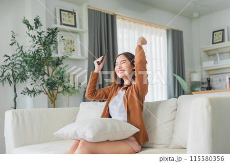 Happy young asian woman relax on comfortable couch at home texting messaging on smartphone 115580356